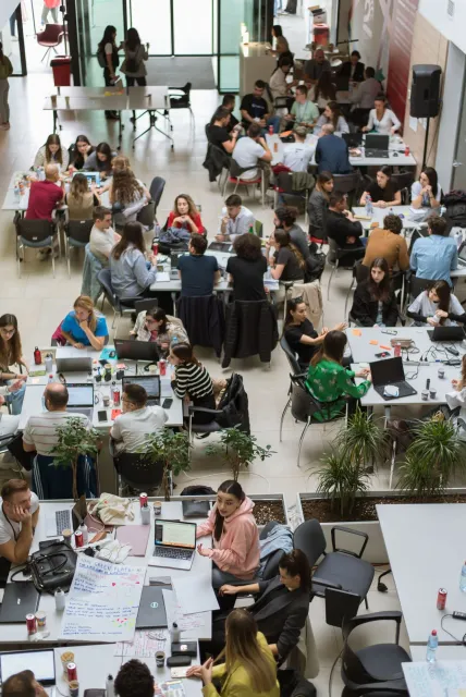 The venue's atrium from above, full of teams working at tables