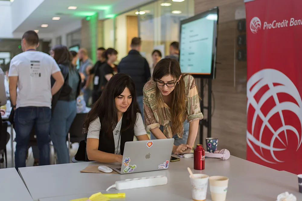 Two participants working together on a laptop at a team table