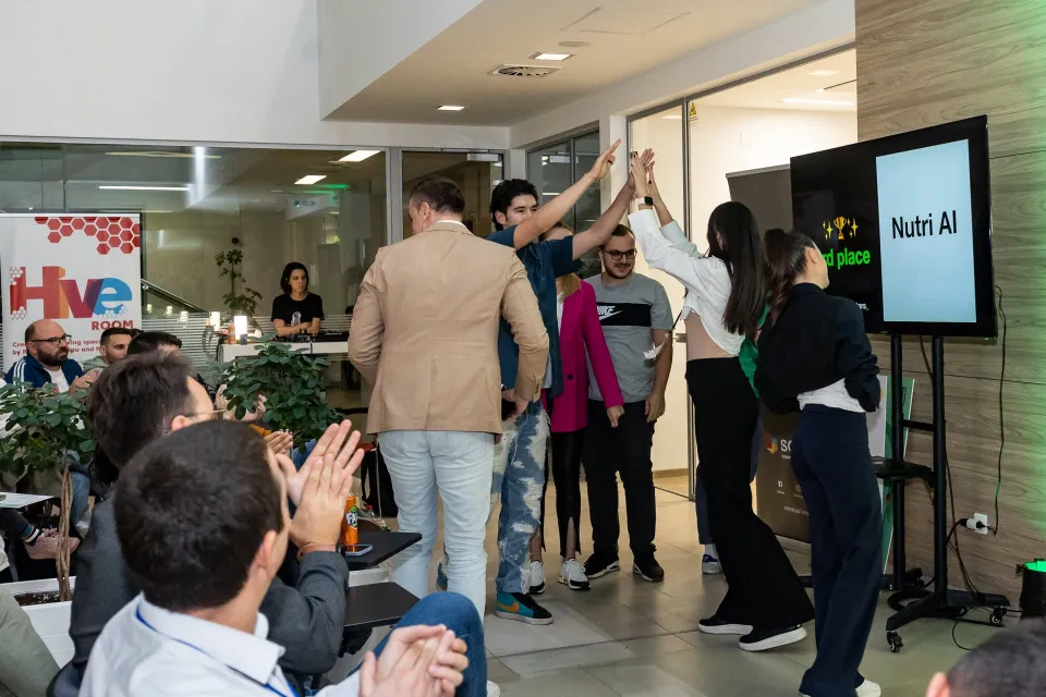 The third-place team high-fiving in front of the screen as the room applauds